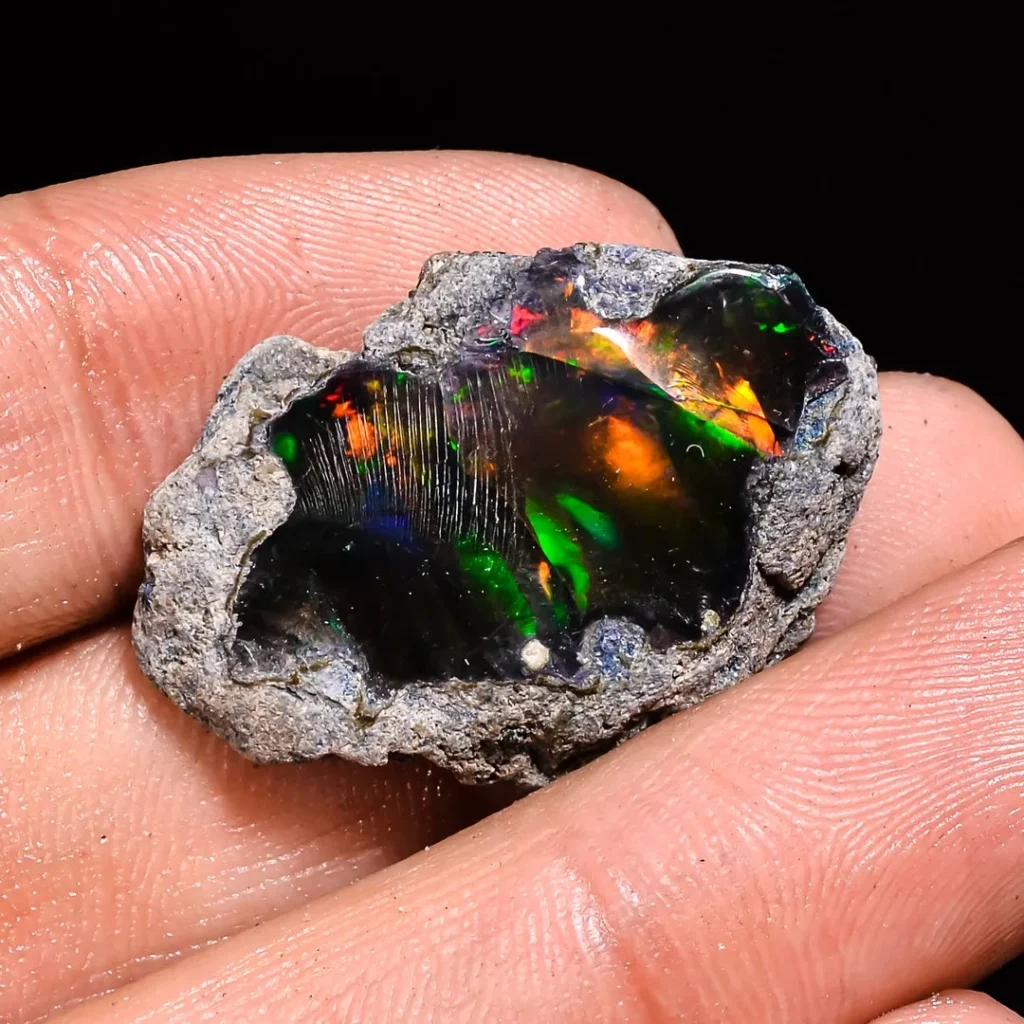 Person holding a rough black opal specimen with vibrant red fire and green play-of-color.