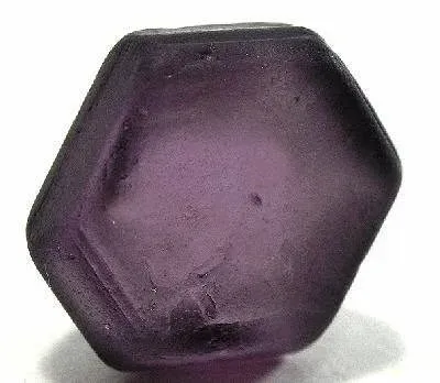 Hexagonal raw purple Taaffeite gemstone crystal resting on a light surface.