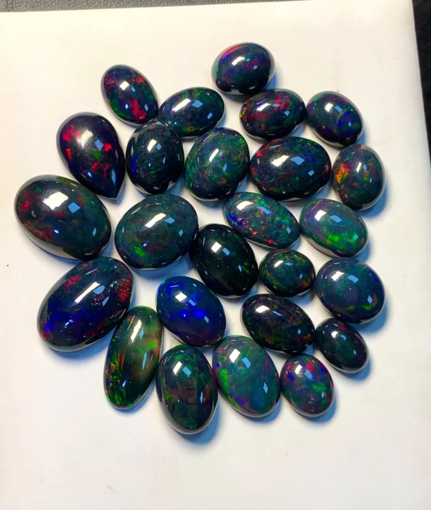 Collection of loose polished black opal cabochons displaying vibrant red, green, and blue play-of-color on a white background.
