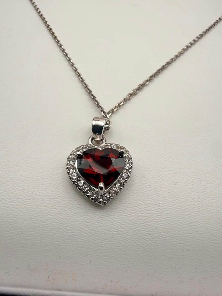 Silver pendant necklace featuring a heart-cut deep red garnet surrounded by a halo of small accent stones.