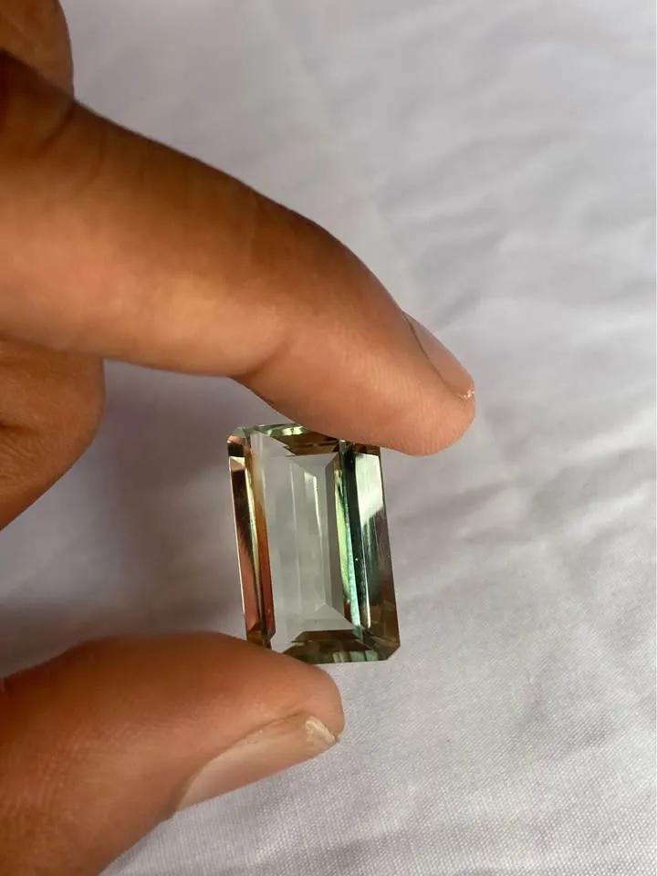 A large rectangular emerald-cut green amethyst (prasiolite) gemstone held between fingers against a plain white background.