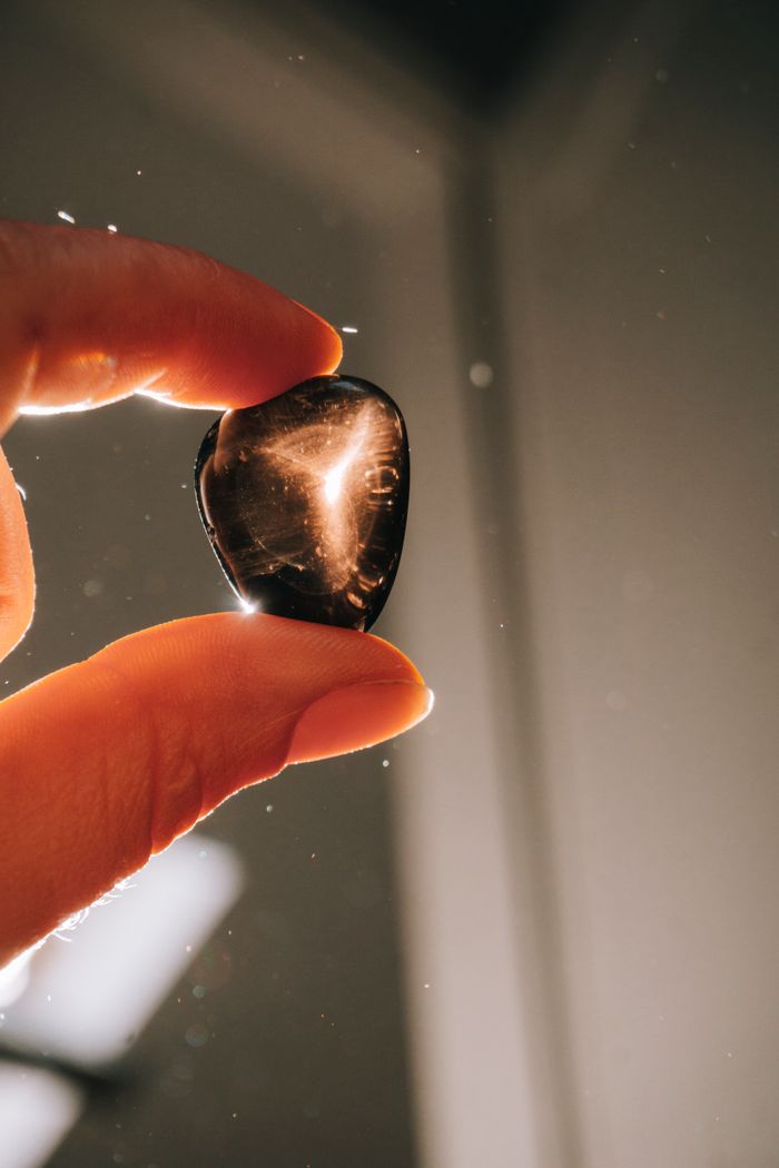 A hand holds a polished obsidian gemstone against a sunlit background, highlighting its reflective surface.