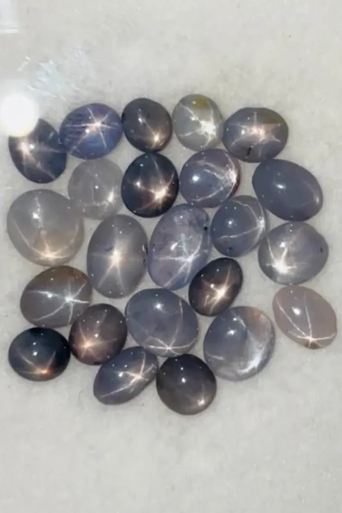 A collection of polished natural star sapphire cabochons showing distinct six-ray asterism stars under bright lighting.