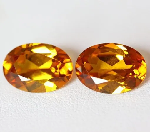 A pair of faceted oval-cut natural golden yellow spinel gemstones side-by-side on a light background.