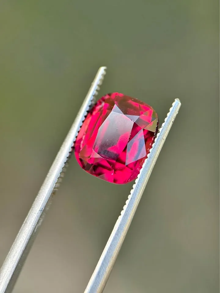 Cushion-cut natural rhodolite garnet gemstone displaying rich raspberry pink and purplish-red brilliance.