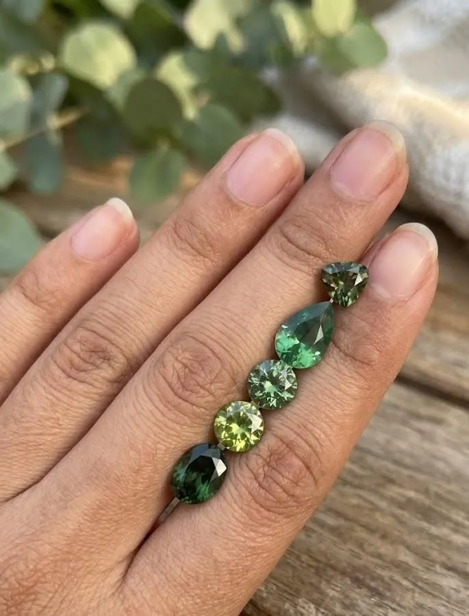 Collection of natural green zircon gemstones in mixed shapes and vibrant green shades shown on a hand.