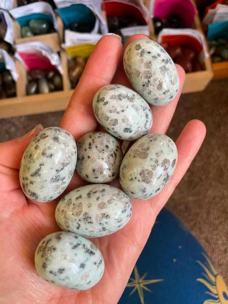Natural polished kiwi jasper tumbled stones and palm pebbles featuring pale mint green matrix with black tourmaline inclusions for crystal healing.