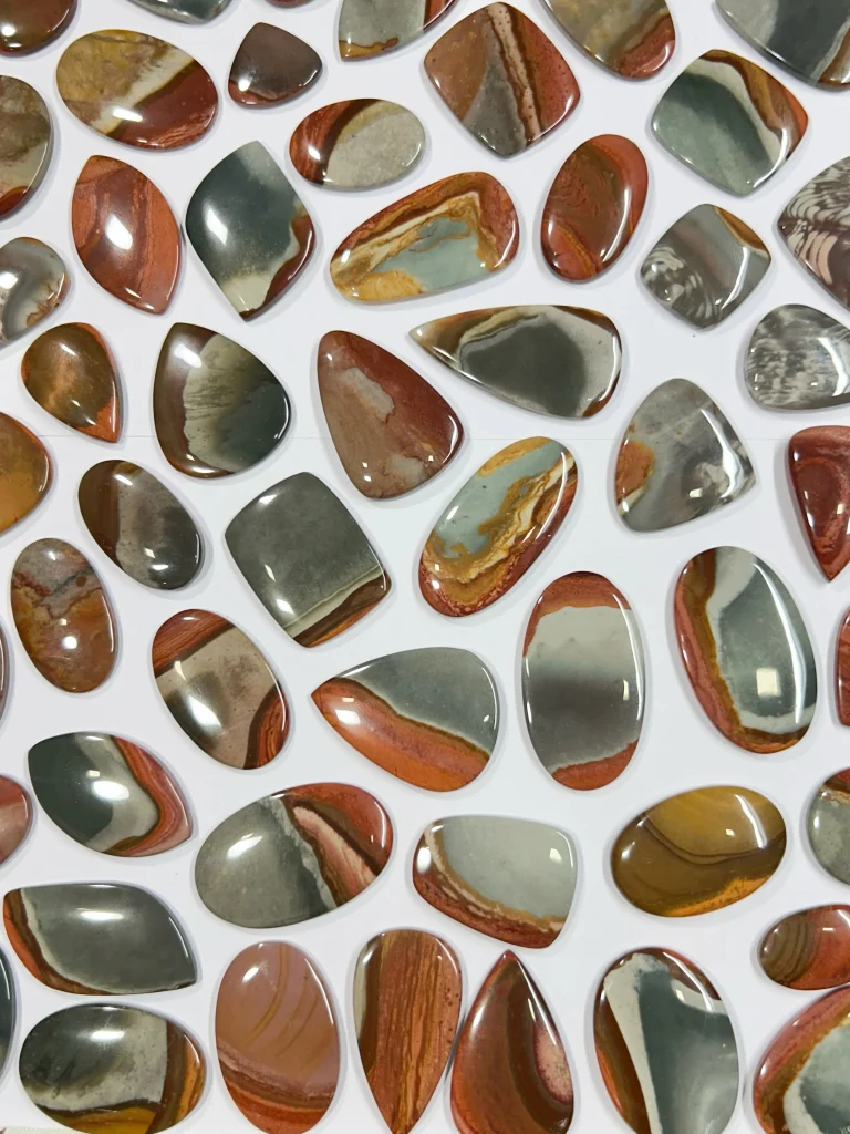 Wholesale lot of natural polished polychrome jasper flat-back cabochons showing terracotta red, sage green, and desert beige banded patterns for jewelry making.