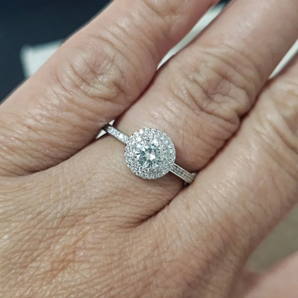 Round brilliant moissanite halo engagement ring in white gold featuring a sparkling micro-pavé halo and accent band for ethical bridal jewelry.